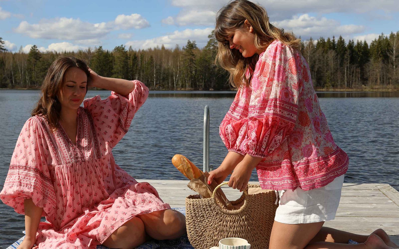Två kvinnor i rosa sommarklänningar äter frukost tillsammans på en brygga