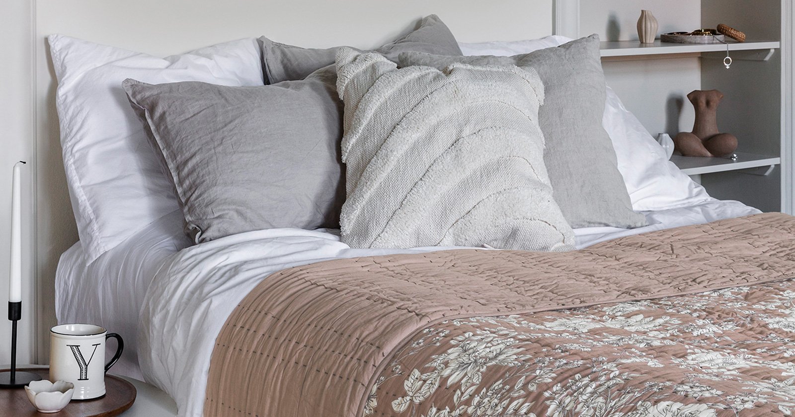 A bed with fluffy pillows in light colours. A quilted, patterned dusty pink bedspread from Indiska is placed on the bed
